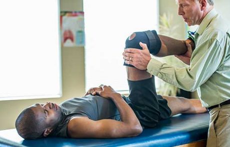 Male chiropractor examining male athlete’s knee Male chiropractor examining male athlete's knee to deliver chiropractic care