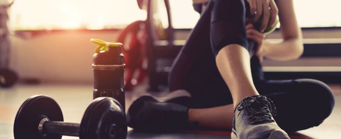 Woman sitting on the floor in a gym with weights and a water bottle