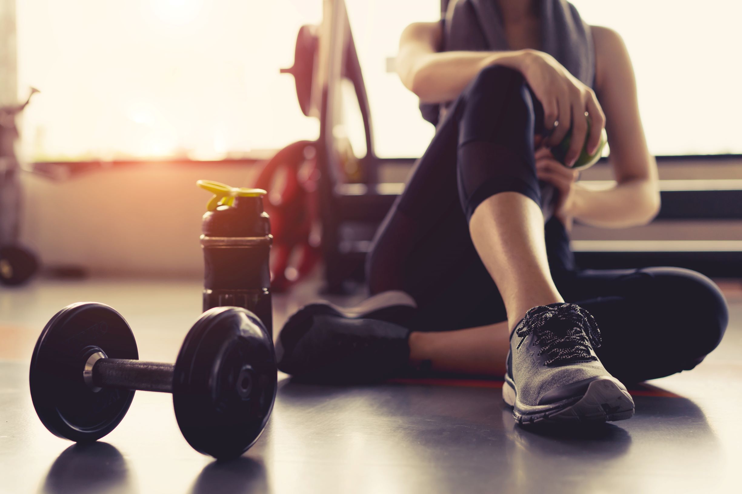 Woman sitting on the floor in a gym with weights and a water bottle