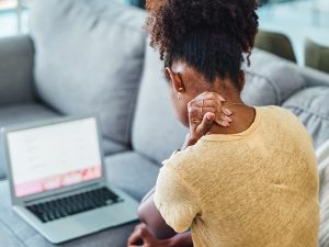 A woman sitting behind a laptop, with her hand on the back of her neck
