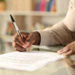 Black man hands signing document on a desk at home Black man hands signing document on a desk at home