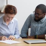 Female signing job contract sitting together with company owner