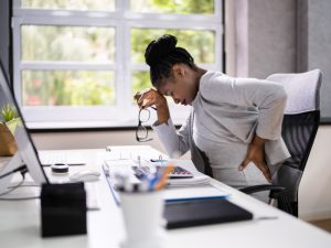 A woman struggles with back pain while sitting at her desk.