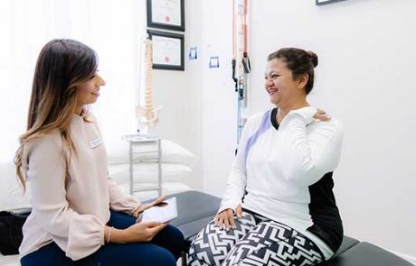 Female chiropractor with female patient pointing to her shoulder Female chiropractor delivering chiropractic care to female patient pointing to her shoulder